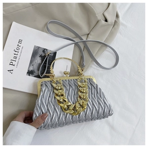 Detail van zilveren geplooide tas met gouden kogelvouwsluiting en grove metalen ketting