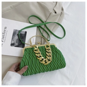 Detail van groene geplooide tas met goudkleurige metalen sluiting en grove ketting