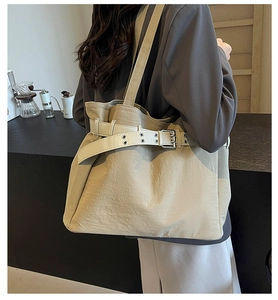 Detail of beige tote bag featuring adjustable belt-style shoulder strap and silver buckle