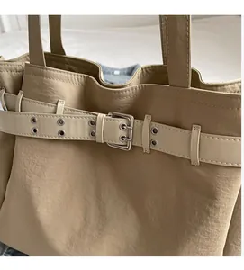 Close-up of decorative metal belt buckle and eyelet details on khaki canvas tote bag