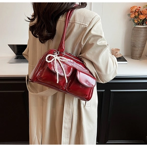 Detail of burgundy patent leather Boston bag with pearl bow charm and dual front pockets
