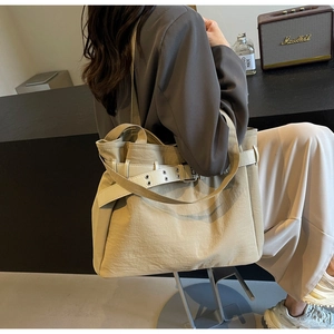 Close-up of beige nylon tote bag featuring a decorative belt buckle and silver hardware