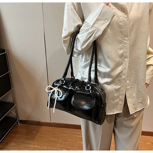 Détail d'un sac à main noir brillant avec breloque nœud en perles et poches avant