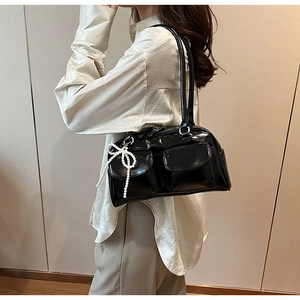 Detail of black glossy leather Boston bag featuring dual flap pockets and a pearl bow charm
