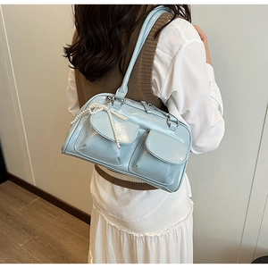 Sac à épaule en cuir verni bleu clair avec nœuds en perles porté par mannequin