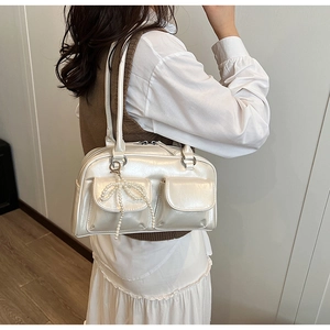 Detail of creamy white Boston bag featuring dual front pockets and pearl bow charm