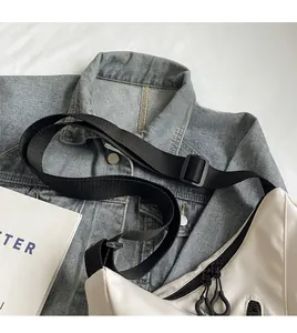 Detail of white canvas crossbody bag with adjustable black nylon strap on denim jacket