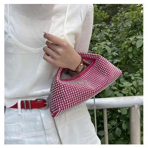 Woman wearing a bright pink rhinestone hobo bag with a silver chain in outdoor sunlight