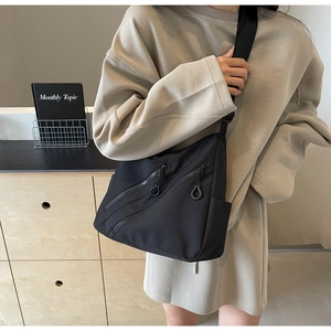 Detail of black nylon tote bag featuring front diagonal zippers and adjustable wide strap