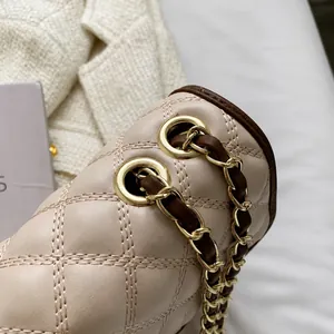 Dettaglio dell'occhiello dorato e della tracolla a catena della borsa beige trapuntata