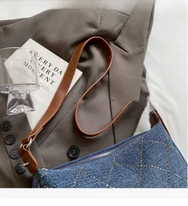 Dettaglio borsa di jeans blu con borchie argentate su blazer marrone e libri d'epoca