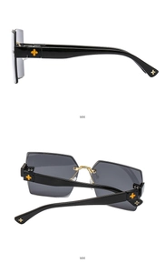 Detail view of black rimless sunglasses featuring golden cross metal temple ornaments