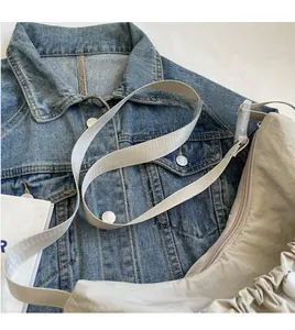Detail view of beige nylon crossbody bag with adjustable strap on denim background