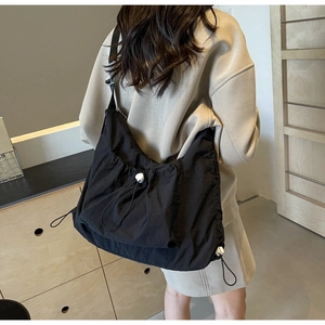 Detail of black nylon crossbody bag featuring stylish drawstring pleats and white toggle beads
