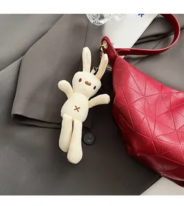 Close-up of white plush bunny charm with metal hook on a red textured handbag