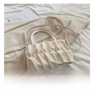 Detailed view of cream ruched cloud bag showing pleated texture on soft fabric background
