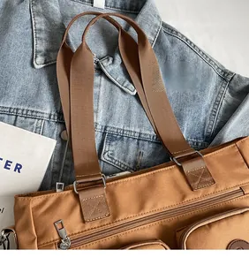 Detail of wide shoulder strap and functional zip pockets on brown canvas tote bag