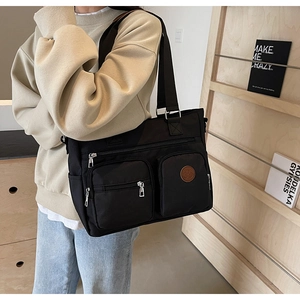 Detail of black large capacity tote bag with front zipper pockets and leather logo patch