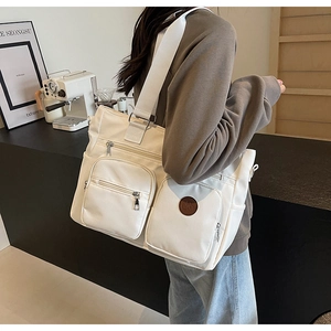 Detail showing two zipper pockets and round logo on the off-white nylon tote bag