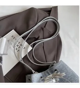 Detail of silver bucket bag with denim texture on dark brown blazer in a lifestyle setting