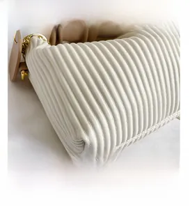 Détail de la texture plissée blanche du sac avec bandoulière brune et chaîne dorée