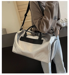 Detalle de un bolso de viaje plateado metalizado grande con asas y correa negra