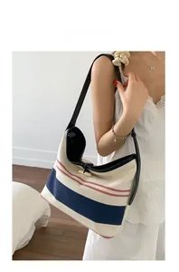 Striped canvas tote bag with wooden toggle clasp shown on model in a cozy indoor setting
