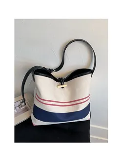 Detail of canvas bucket bag featuring red and navy stripes with a black leather horn button