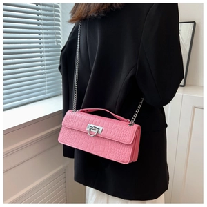 Detailed shot of pink crocodile pattern small square bag with silver chain worn by model