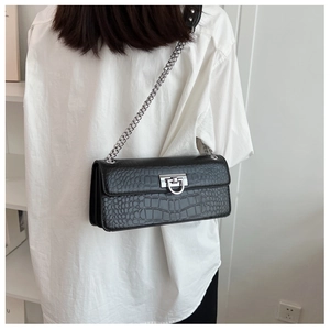 Detail of black faux leather bag with crocodile texture and silver chain strap on model