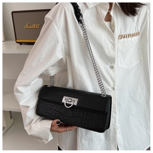 Detail of black crocodile pattern baguette bag with silver buckle and chain strap