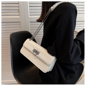 Detail of white crocodile embossed texture on crossbody bag with silver chain strap