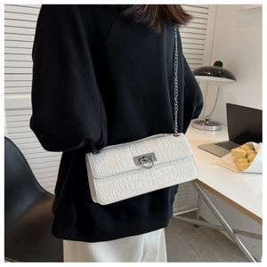 Detail of white crocodile pattern baguette bag with silver chain strap on model