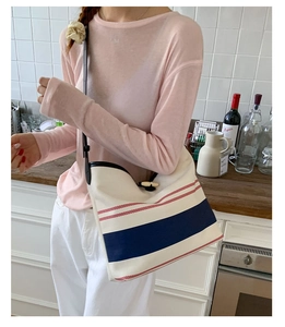 Detail of striped canvas tote bag with black leather shoulder straps and ring hardware