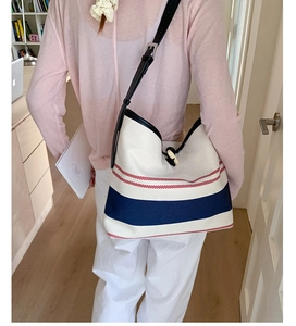 Detail view of striped canvas bucket bag with leather strap and horn button closure