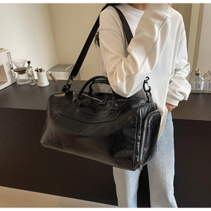 Gran bolsa de viaje de cuero sintético negro brillante, llevada por una modelo.