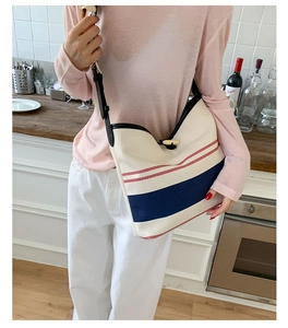 Detail of striped canvas tote bag with leather trim and wooden buckle on a model