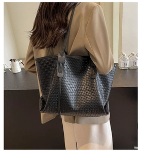 Detailed view of black woven tote bag with crossbody strap on a beige suit model