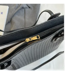 Macro detail of golden metal zipper and black woven texture on minimalist PU handbag