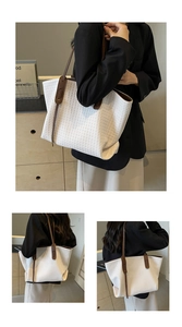 Close-up of white woven tote bag featuring brown leather straps and spacious interior