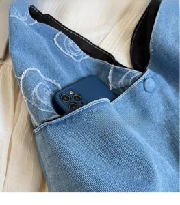 Detail of denim tote bag showing functional side pocket with rose pattern embroidery
