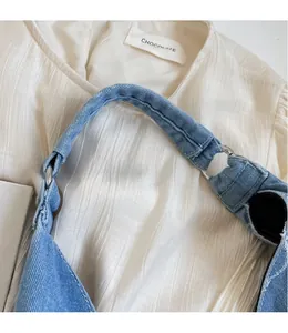 Detail of blue denim handbag wide shoulder strap with silver metal ring connector