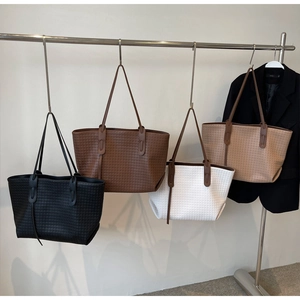 Four minimalist woven tote bags in black, white, coffee, and khaki hanging on a display rack