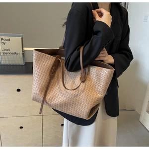 Large beige woven tote bag with dark brown leather handles on a model in a minimal setting