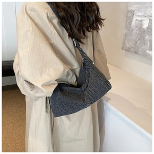 Detail of dark grey textured denim hobo bag worn by model over a beige trench coat