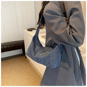 Detailed view of blue denim texture hobo bag worn by model in a modern interior setting