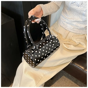 Detailed view of a black cylindrical barrel bag with white polka dots in glossy patent leather