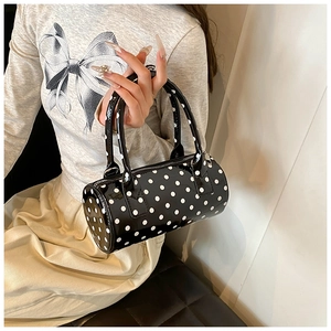 Polka dot cylindrical handbag in black patent leather shown on model's arm for daily use