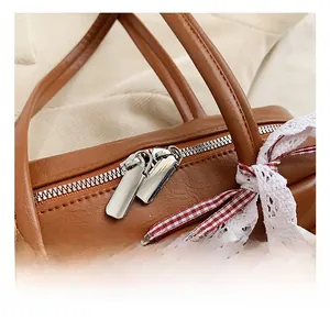 Detail of silver dual zippers and lace bow on caramel brown pebbled PU leather shoulder bag