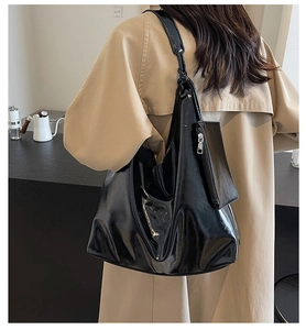 Detail view of black glossy hobo bag with matching mini pouch on beige trench coat